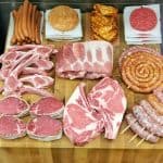 selection of raw beef cuts, sausages, and patties